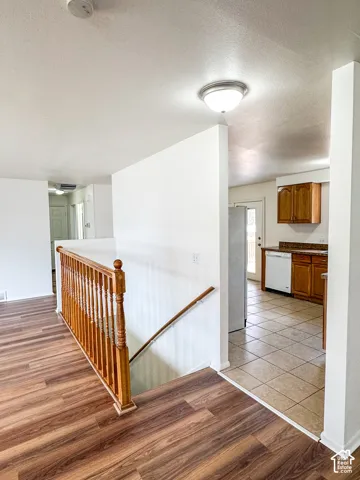 Wood-finish flooring, staircase with wood railing, recessed ceiling light, and kitchen with wood cabinetry and tile flooring