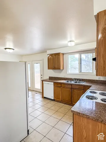 Kitchen featuring tile flooring, wood-finish cabinetry, a double basin stainless steel sink, and a built-in dishwasher