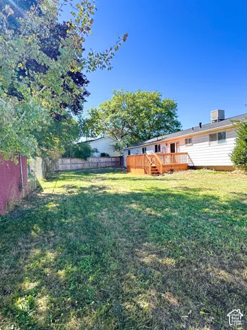 Expansive grass lawn with a wooden privacy fence, mature trees, and a multi-level wood deck
