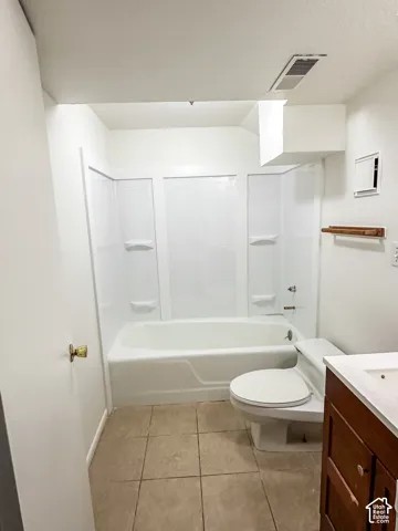Bathtub with white surround, toilet, wood-finish vanity with white sink, and tiled flooring
