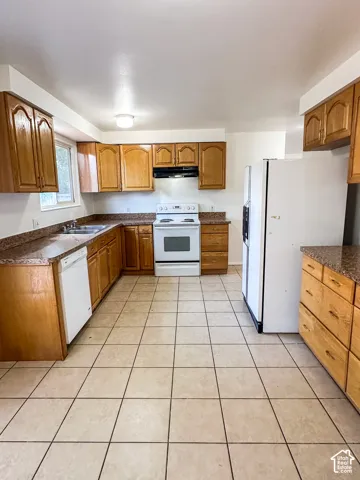 Kitchen featuring wood cabinetry, speckled countertops, tile flooring, and white appliances