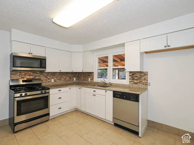 Kitchen featuring white cabinetry, stainless steel appliances, granite-look countertops, a stone-look tile backsplash, and tile flooring
