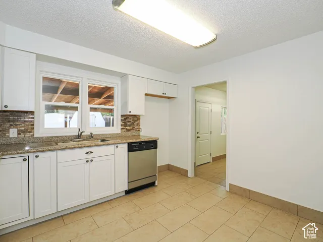 White cabinetry with dark hardware, granite-style countertops, mosaic tile backsplash, stainless steel dishwasher, and tiled flooring
