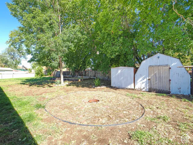 Expansive yard with mature trees, two storage sheds, and a circular ground-level feature
