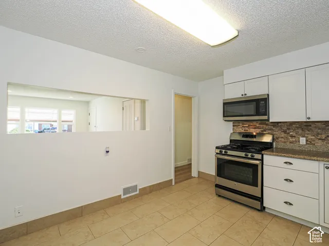 Kitchen featuring tile flooring, white cabinetry, stainless steel oven, stainless steel microwave, and stone-finish backsplash