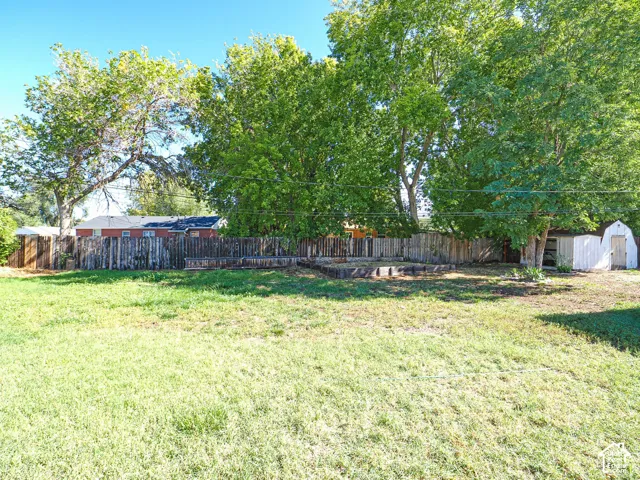 Expansive yard space featuring mature trees, a wood privacy fence, and an outdoor storage shed