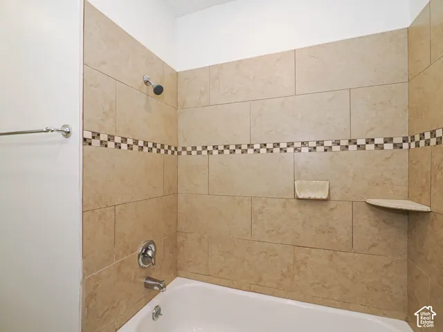 Bathtub and shower combination with full-height tile surround, decorative mosaic tile accent, and built-in corner shelf