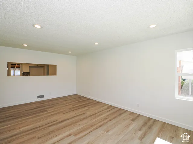 Recessed lighting, wood-finish flooring, white walls, large window, and a pass-through opening