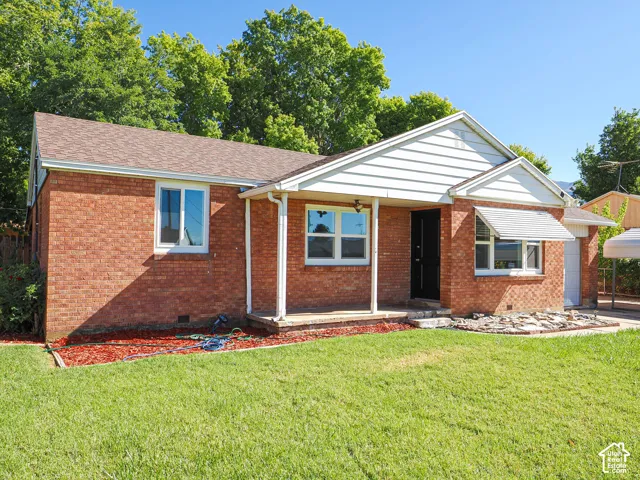 Brick exterior with white trim, covered front porch, asphalt shingle roof, and a manicured lawn