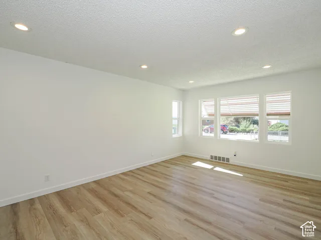 Recessed ceiling lighting, multiple windows with blinds, light wood-finish flooring, and white walls
