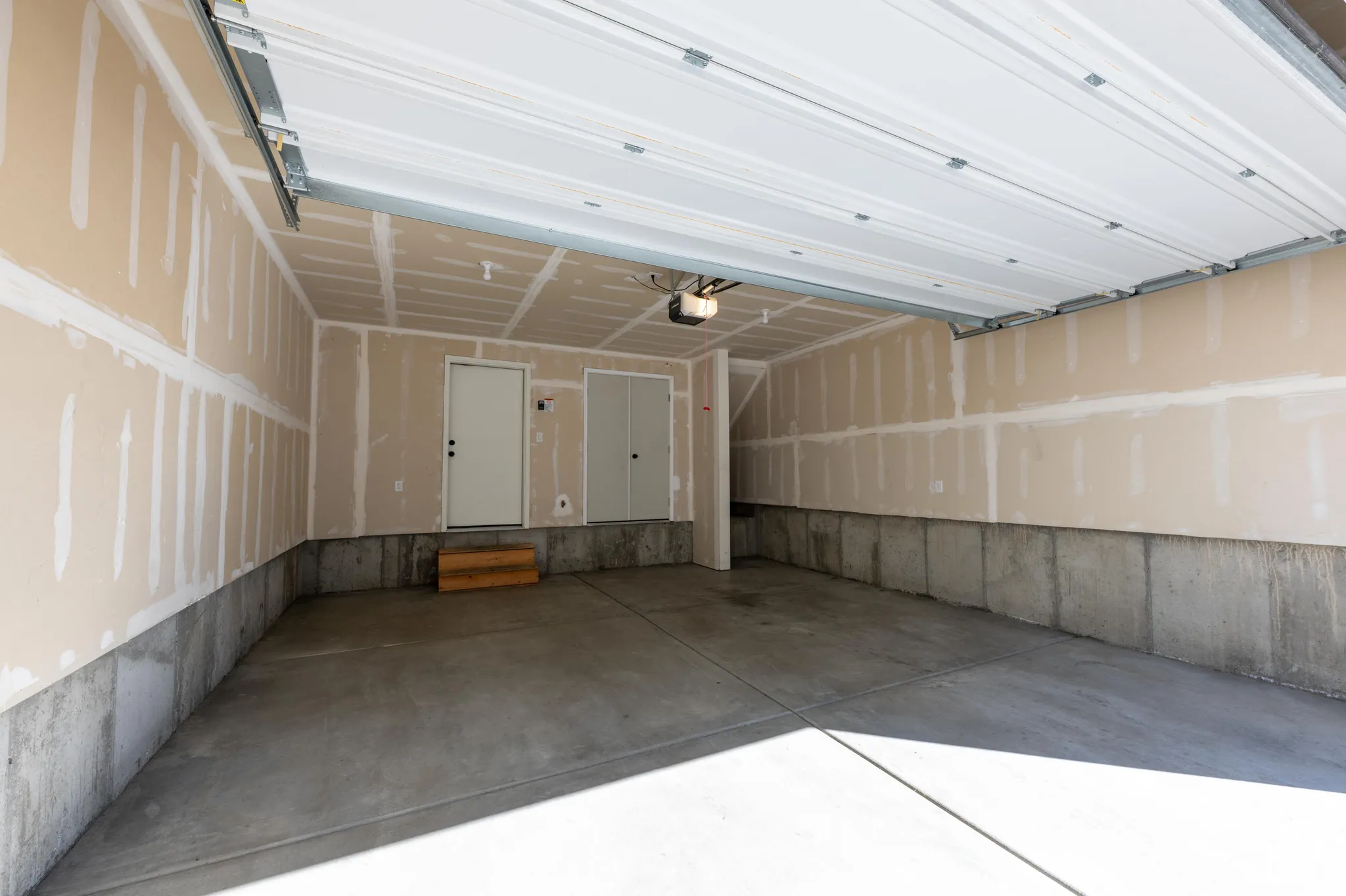 Concrete floor, two doors, exposed drywall, and garage door opener
