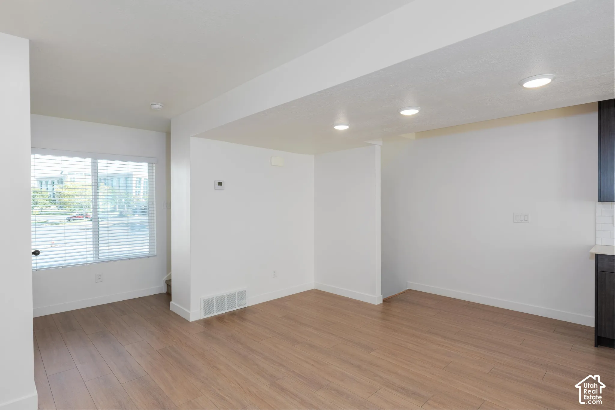 Recessed ceiling lighting, wood-finish flooring, white walls, and a large window with blinds