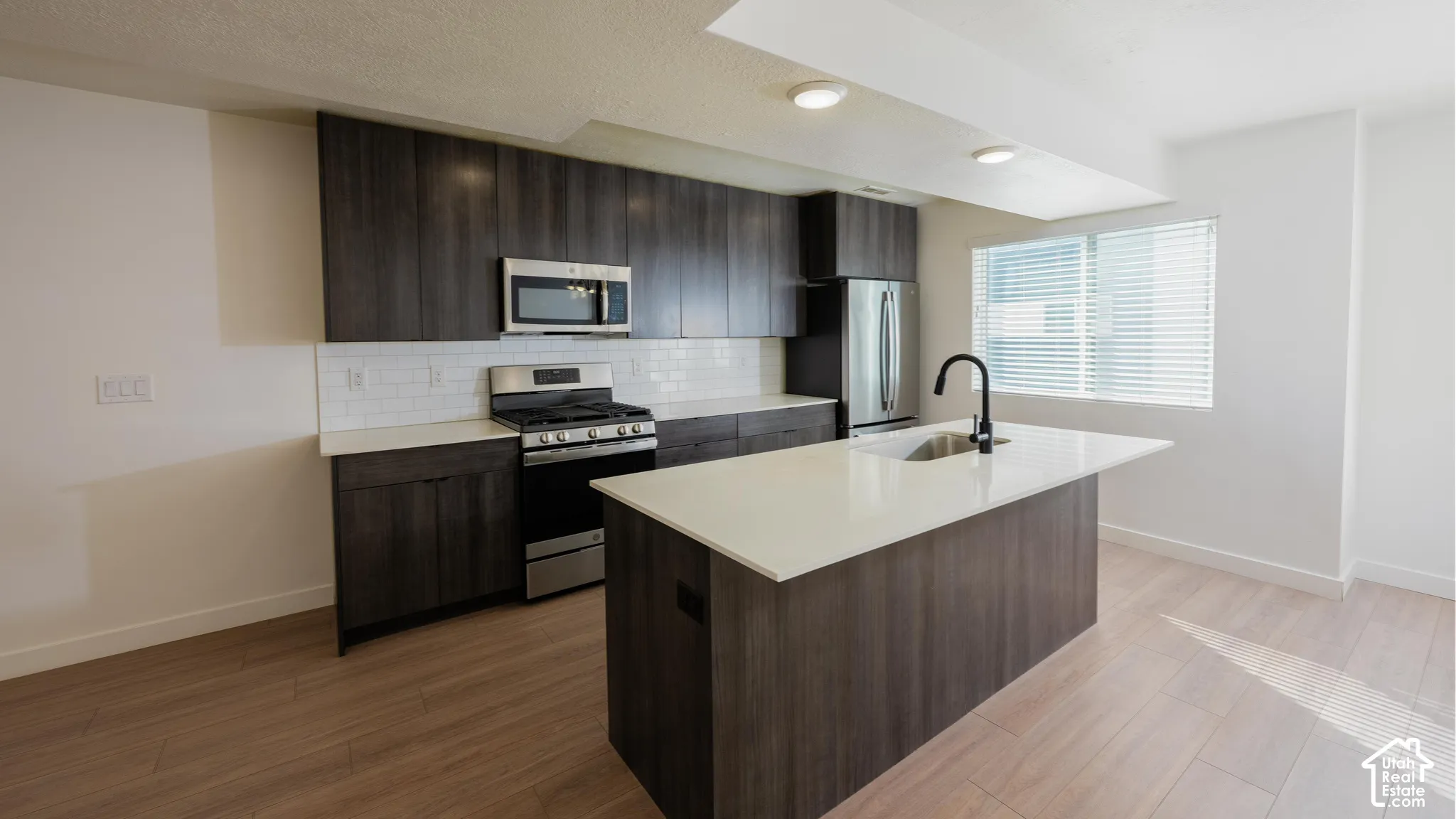 Modern kitchen featuring dark wood-finish cabinetry, white subway tile backsplash, stainless steel appliances, and a central island with a matte black faucet