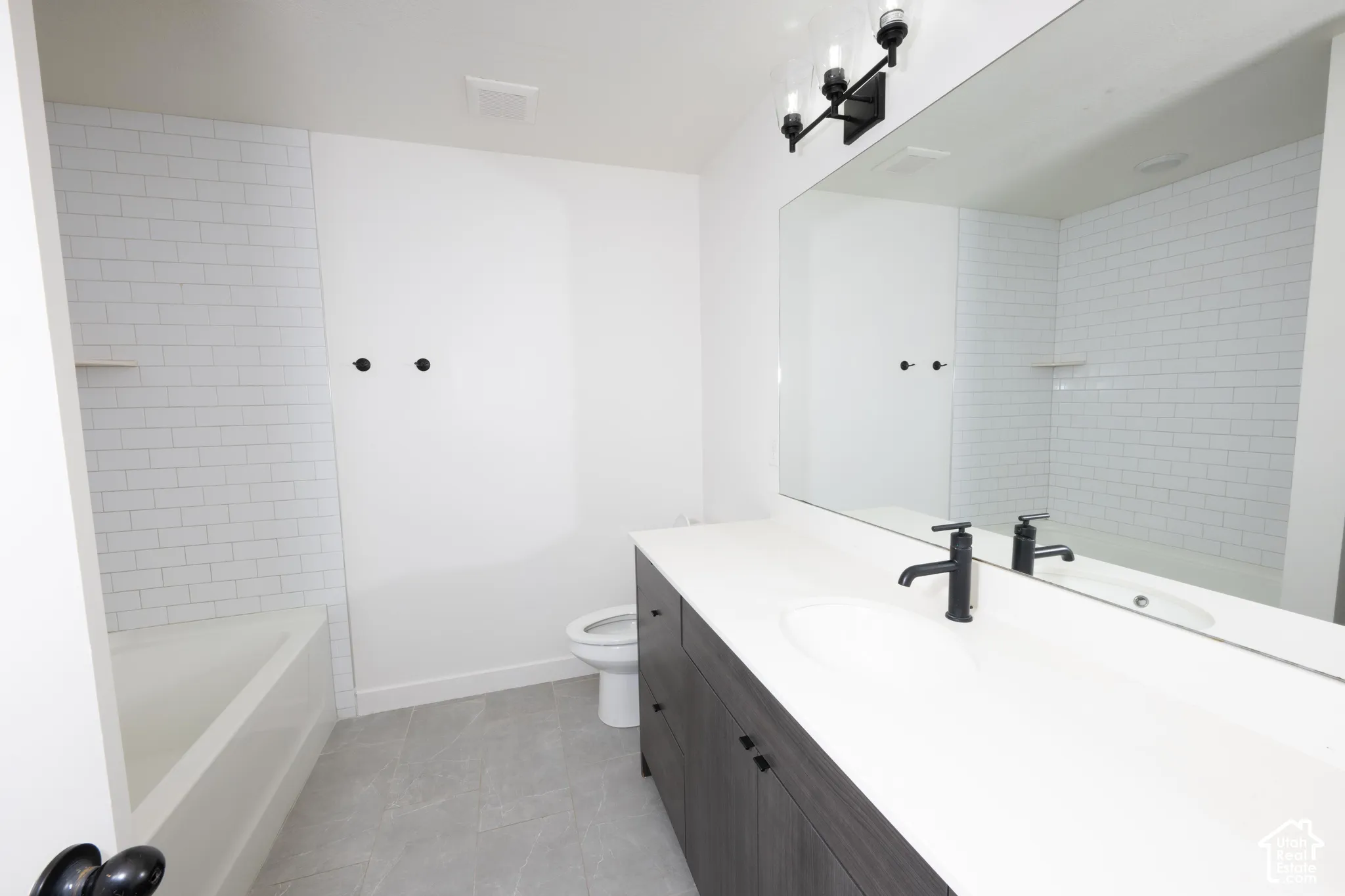 Modern primary bathroom featuring a floating vanity with white quartz countertop, dual vessel sinks with matte black faucets, frameless glass shower enclosure, subway tile walls, and polished concrete flooring