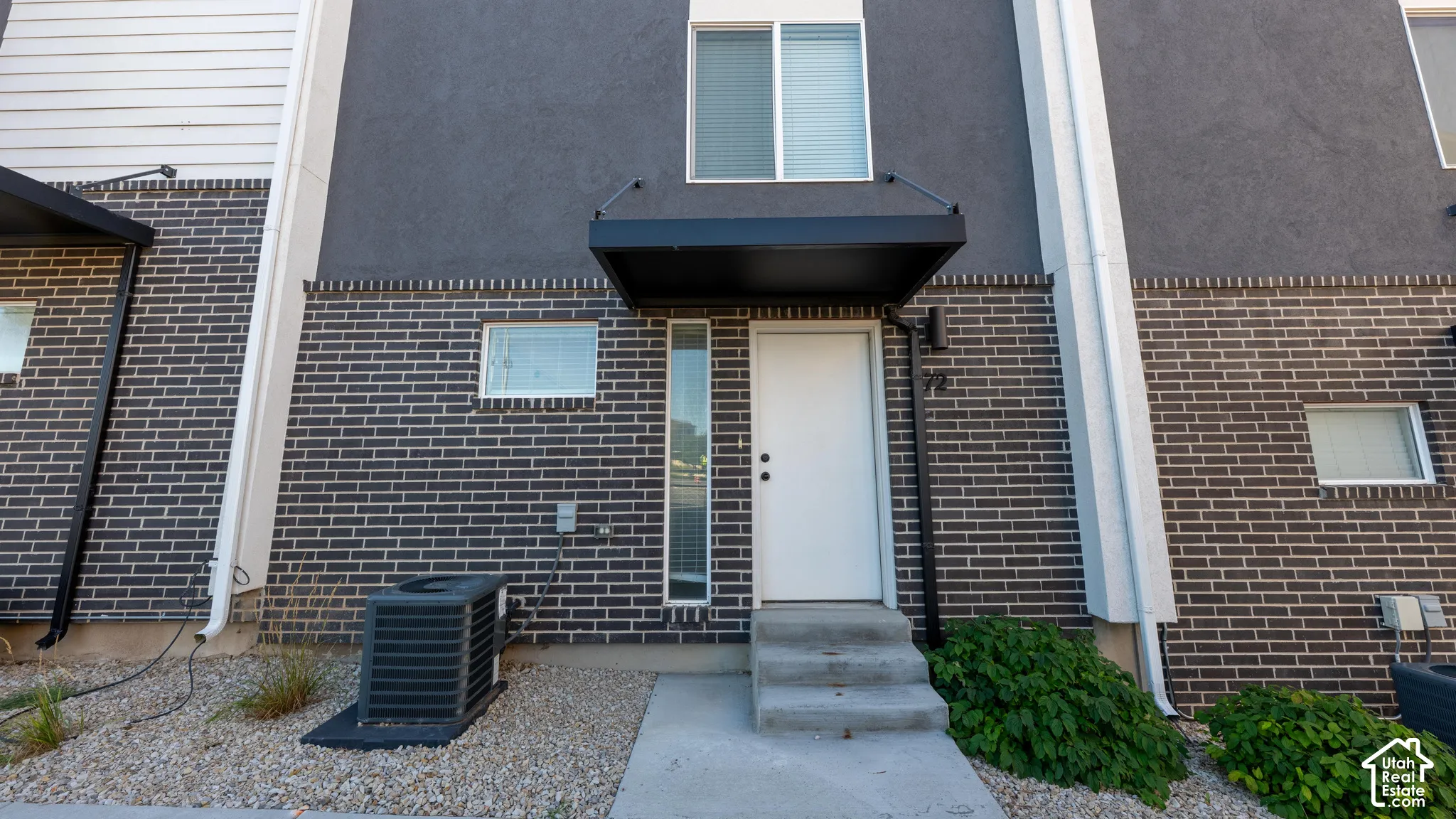 Modern townhouse exterior featuring a dark brick facade, stucco siding, a black awning, and concrete steps