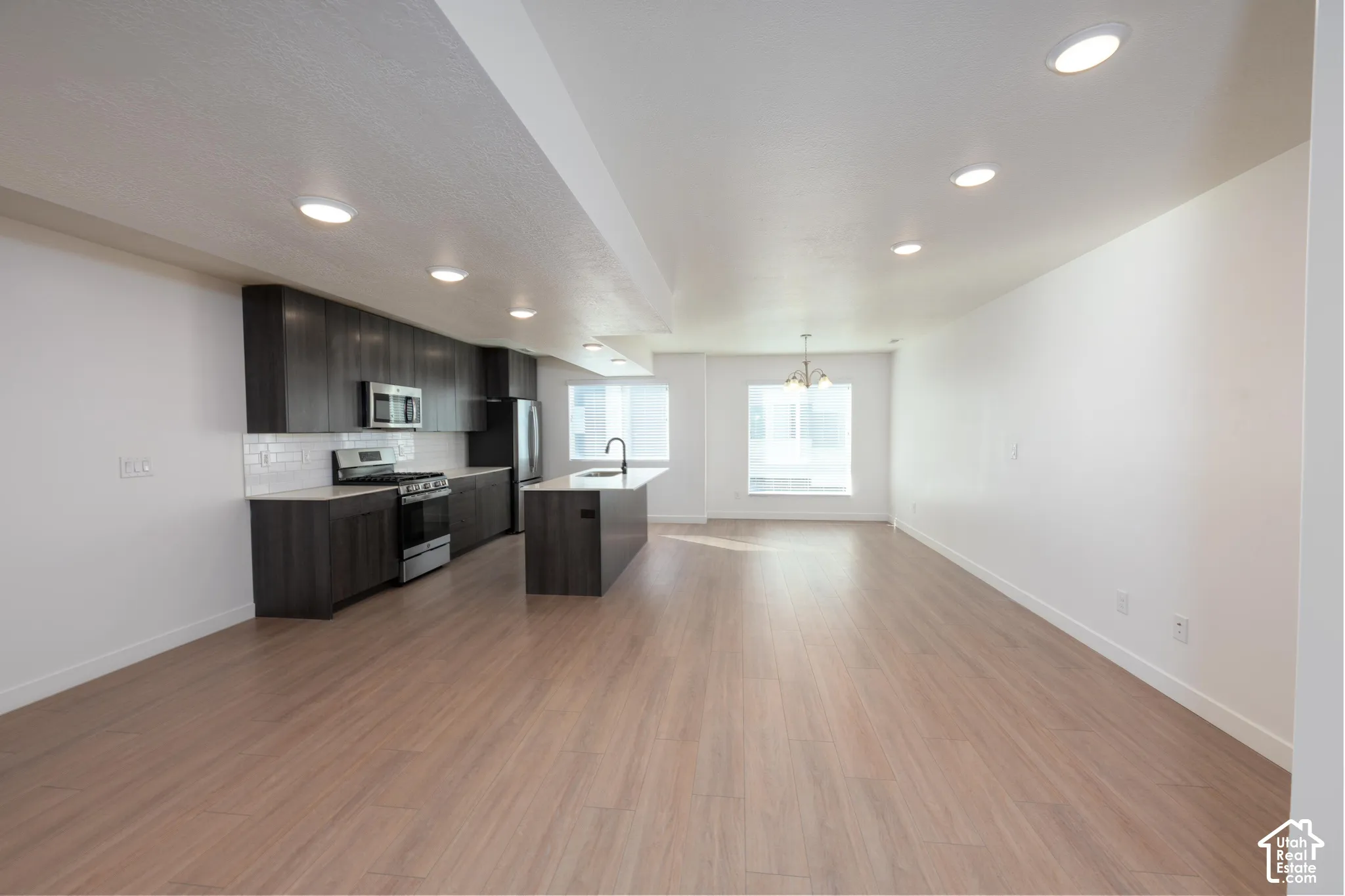 Open-concept living space with wood-finish flooring, recessed lighting, a kitchen island, and stainless steel appliances