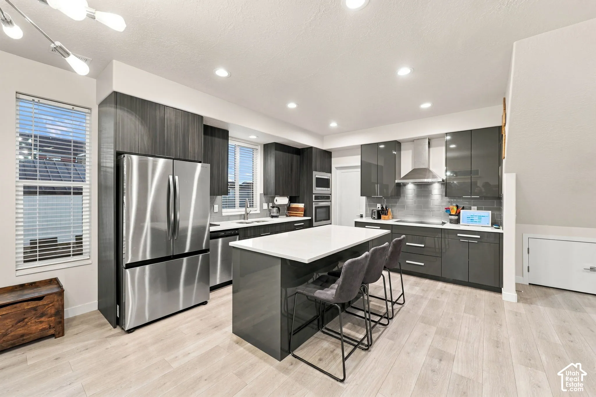 Modern kitchen featuring stainless steel appliances, dark wood-finish cabinetry, a large center island with seating, white countertops, and recessed lighting