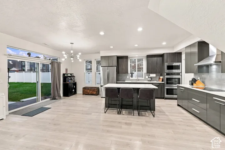 Open-concept living space with light wood-finish flooring, modern kitchen, white countertops, built-in stainless steel appliances, and a sliding glass door to the backyard