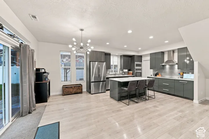 Open-concept living area featuring wood-finish flooring, recessed lighting, a modern chandelier, a kitchen island with seating, and stainless steel appliances