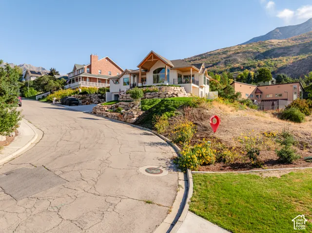 Mountain backdrop, sloped landscaping, stone retaining walls, and a multi-level residence with a wood-accented balcony