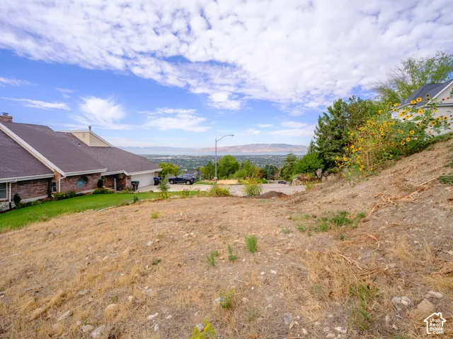 Expansive building lot featuring sloped terrain, natural vegetation, and distant body of water