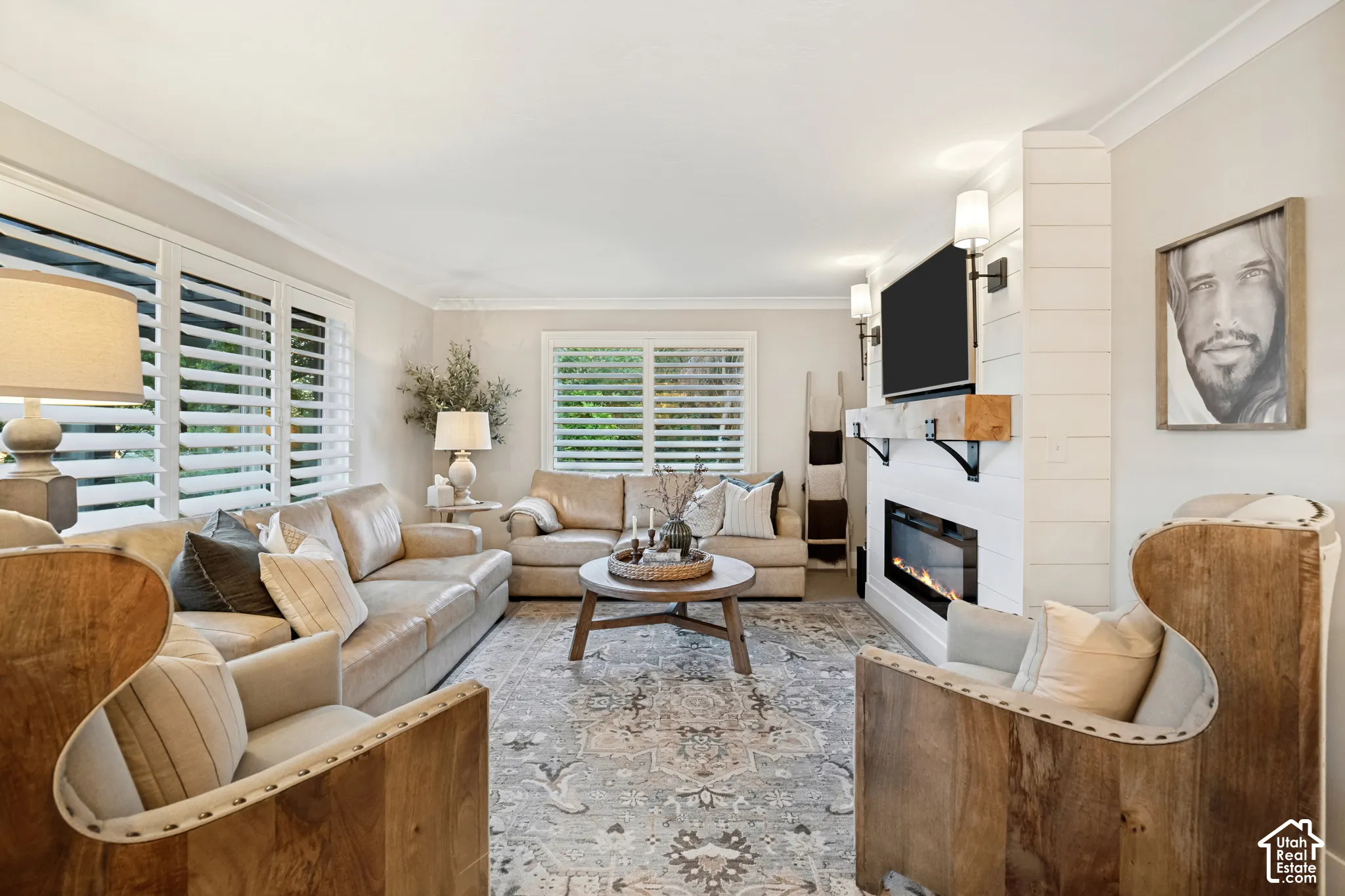 Hardwood-style flooring, white window shutters, crown molding, electric fireplace with shiplap-style surround, and wall-mounted sconces