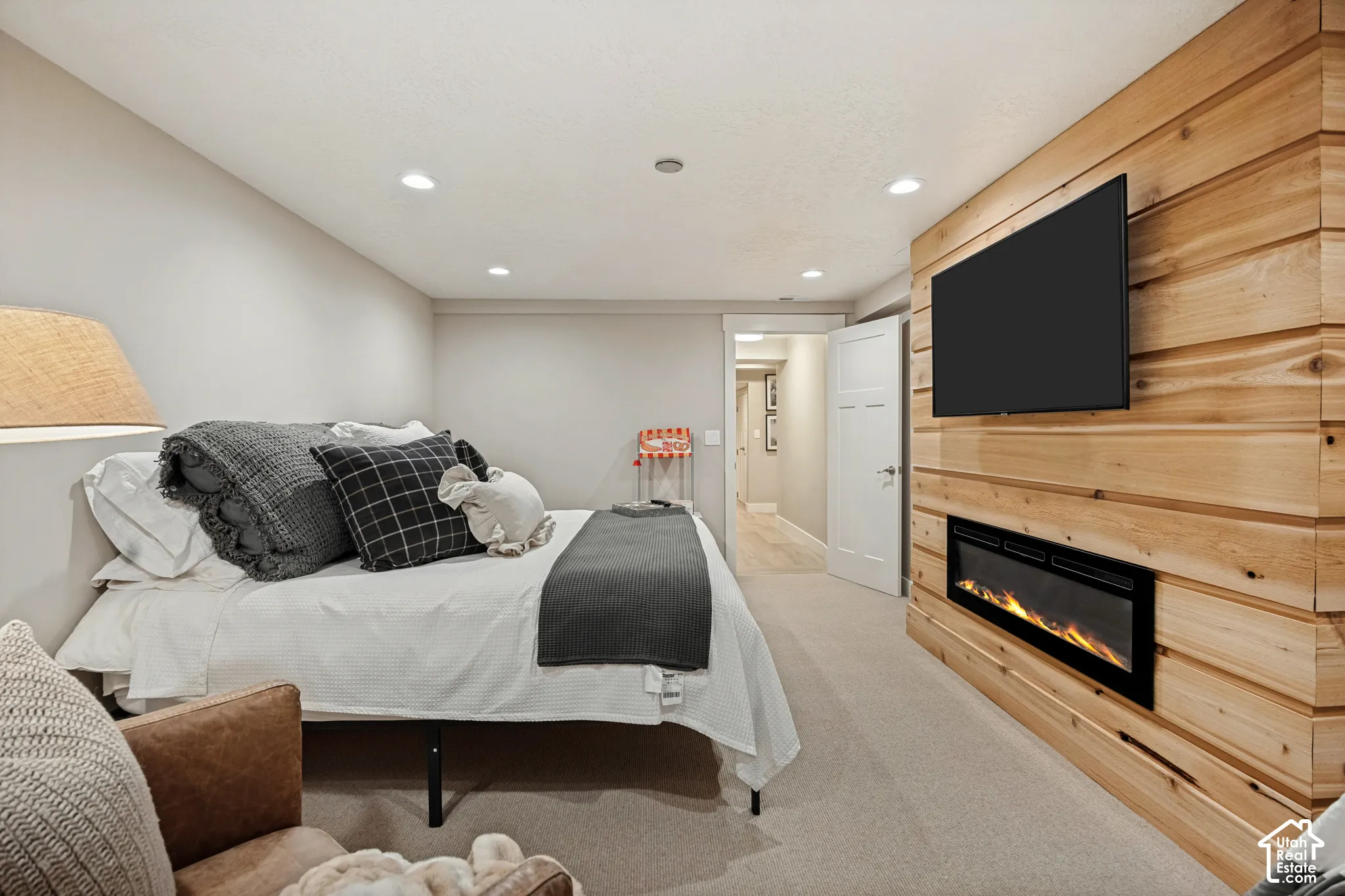 Recessed lighting, wood-paneled accent wall, built-in electric fireplace, wall-mounted television, and neutral carpet flooring