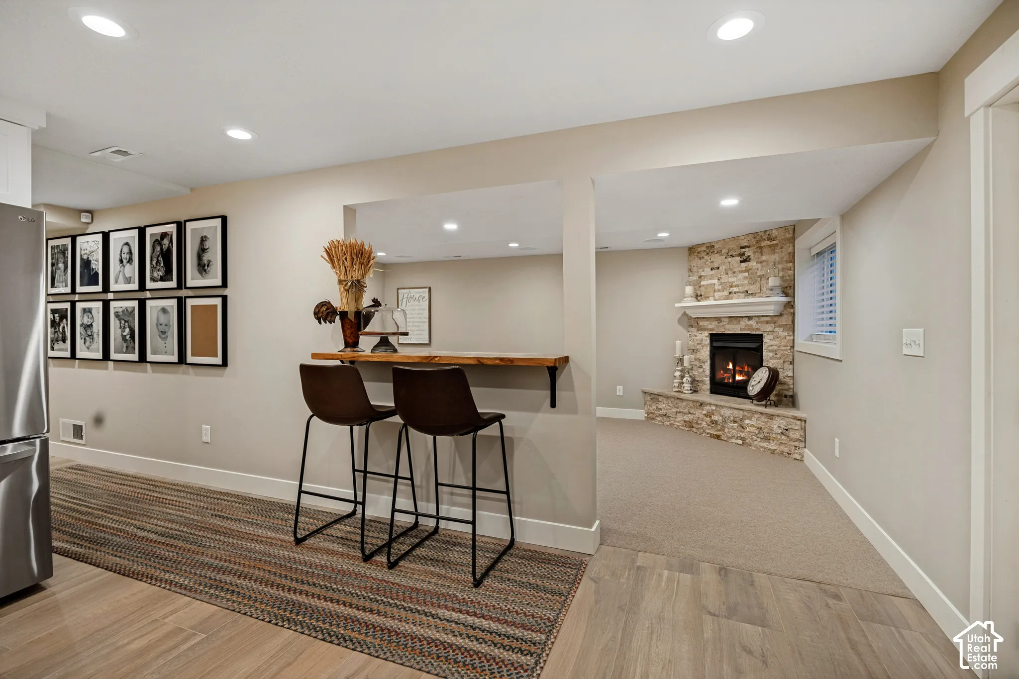 Recessed lighting throughout, wood-finish flooring, built-in bar, stone fireplace surround, and a neutral color palette