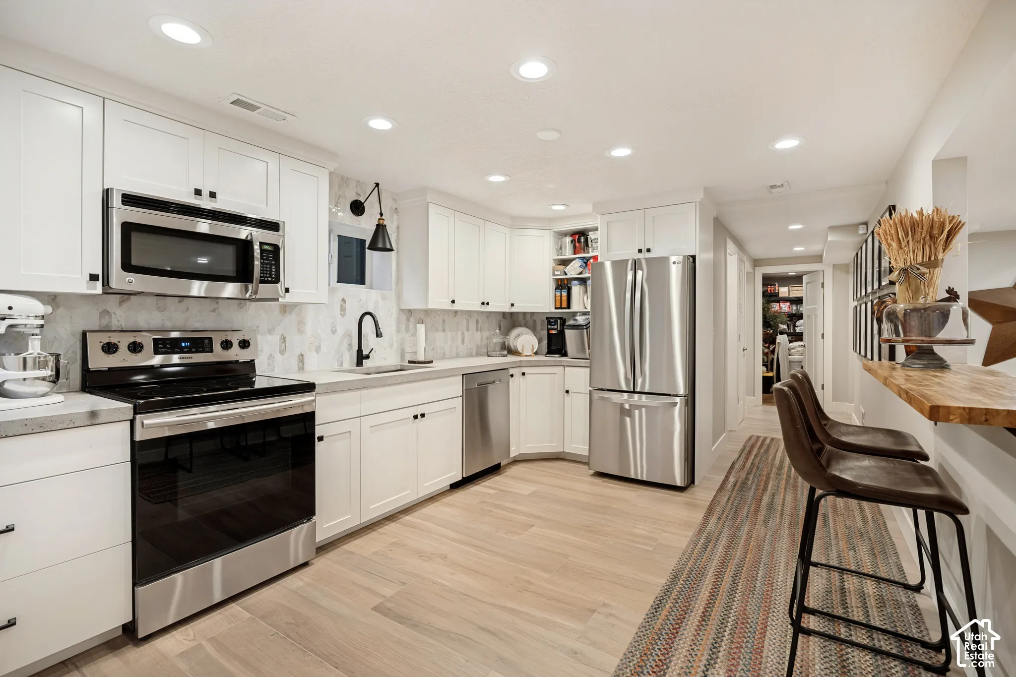 White shaker cabinetry with black hardware, stainless steel appliances, concrete-finish countertops, wood-finish flooring, and recessed lighting