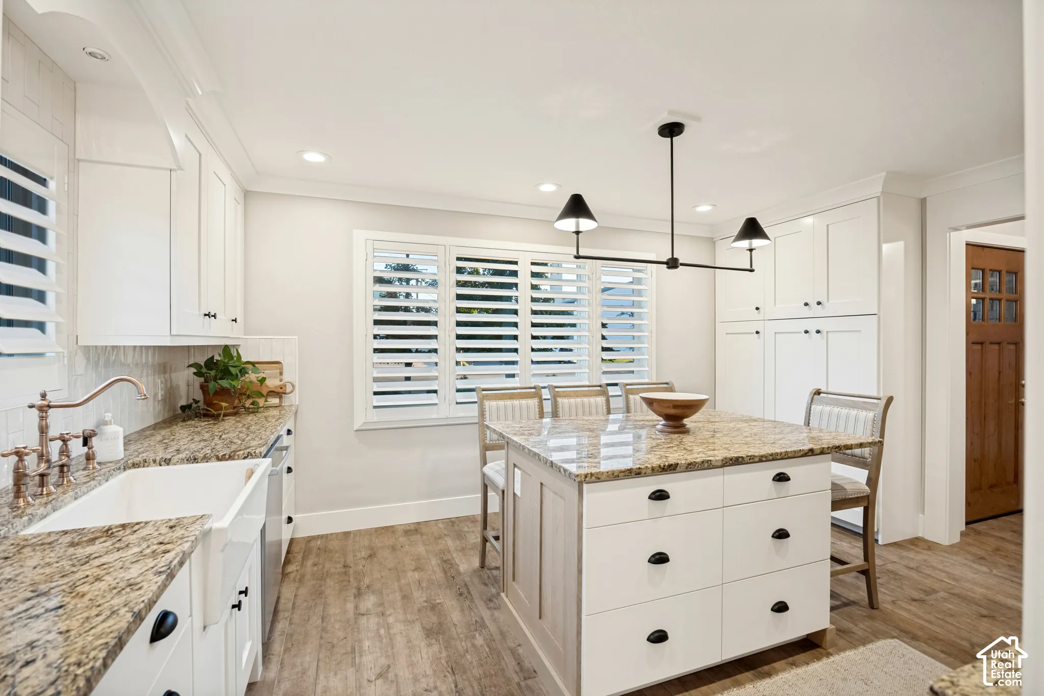 Kitchen featuring white cabinetry, granite countertops, wood-finish flooring, a farmhouse sink, and a central island with seating