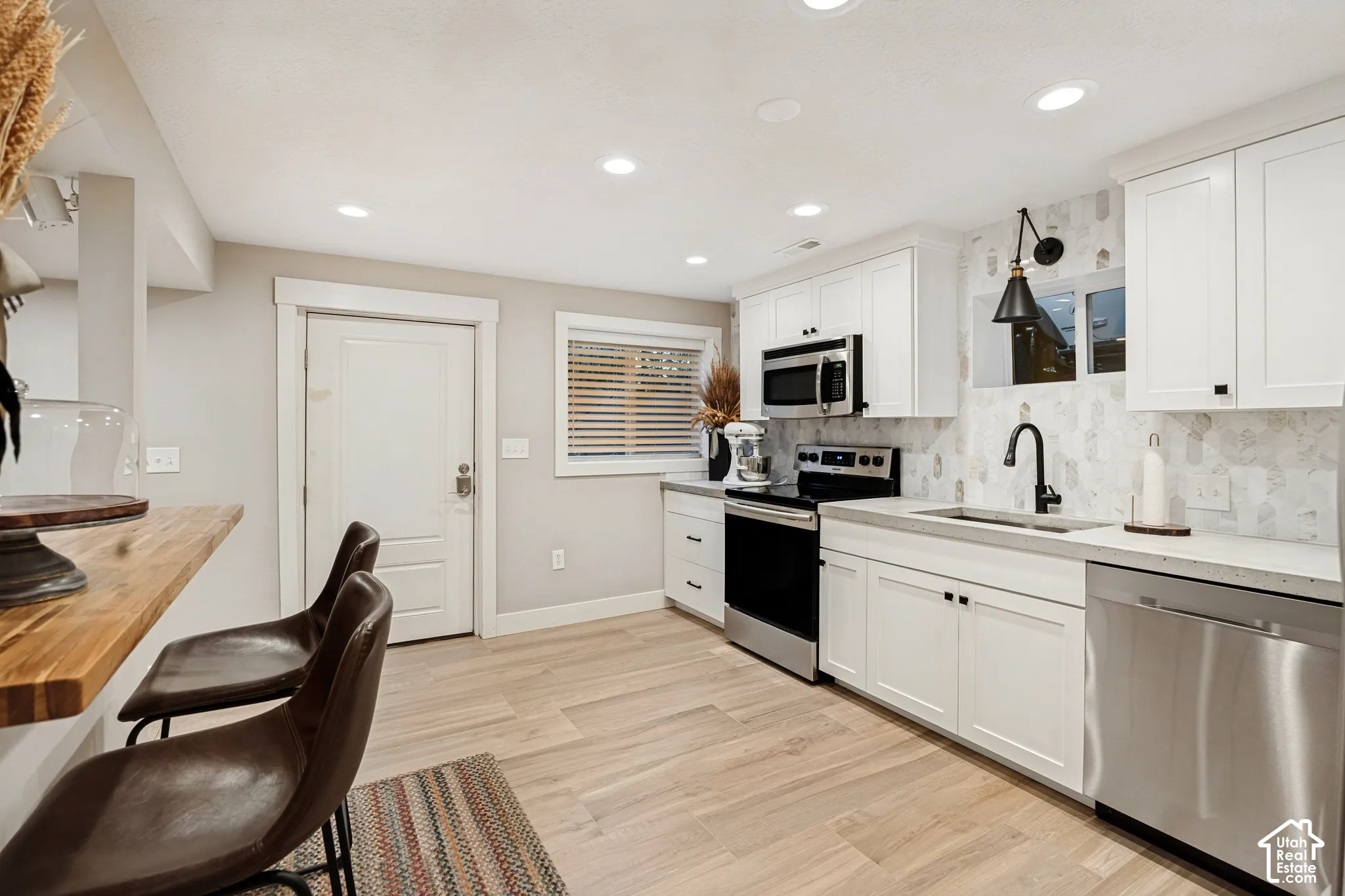 White cabinetry, wood-finish flooring, stainless steel appliances, recessed lighting, and a window with blinds