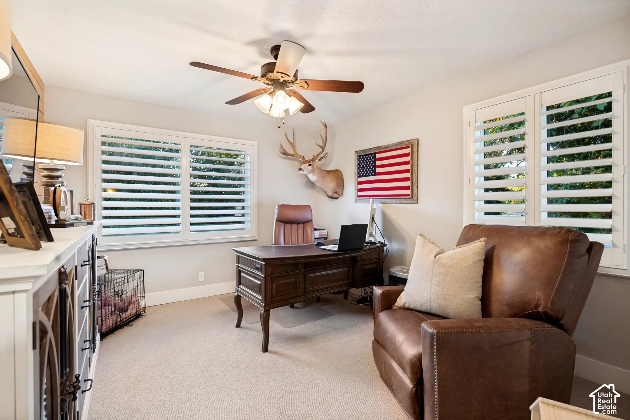 Ceiling fan, two windows with white plantation shutters, and a built-in white cabinet with decorative wood-finish doors