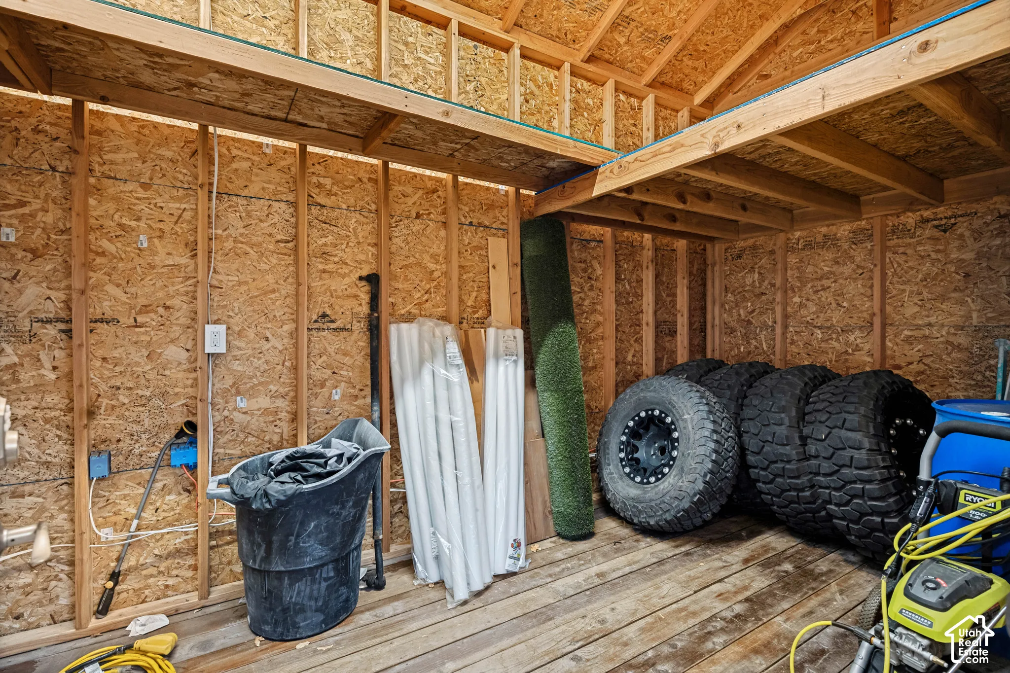 Open stud wall construction with oriented strand board sheathing, exposed electrical outlets, and wood plank flooring