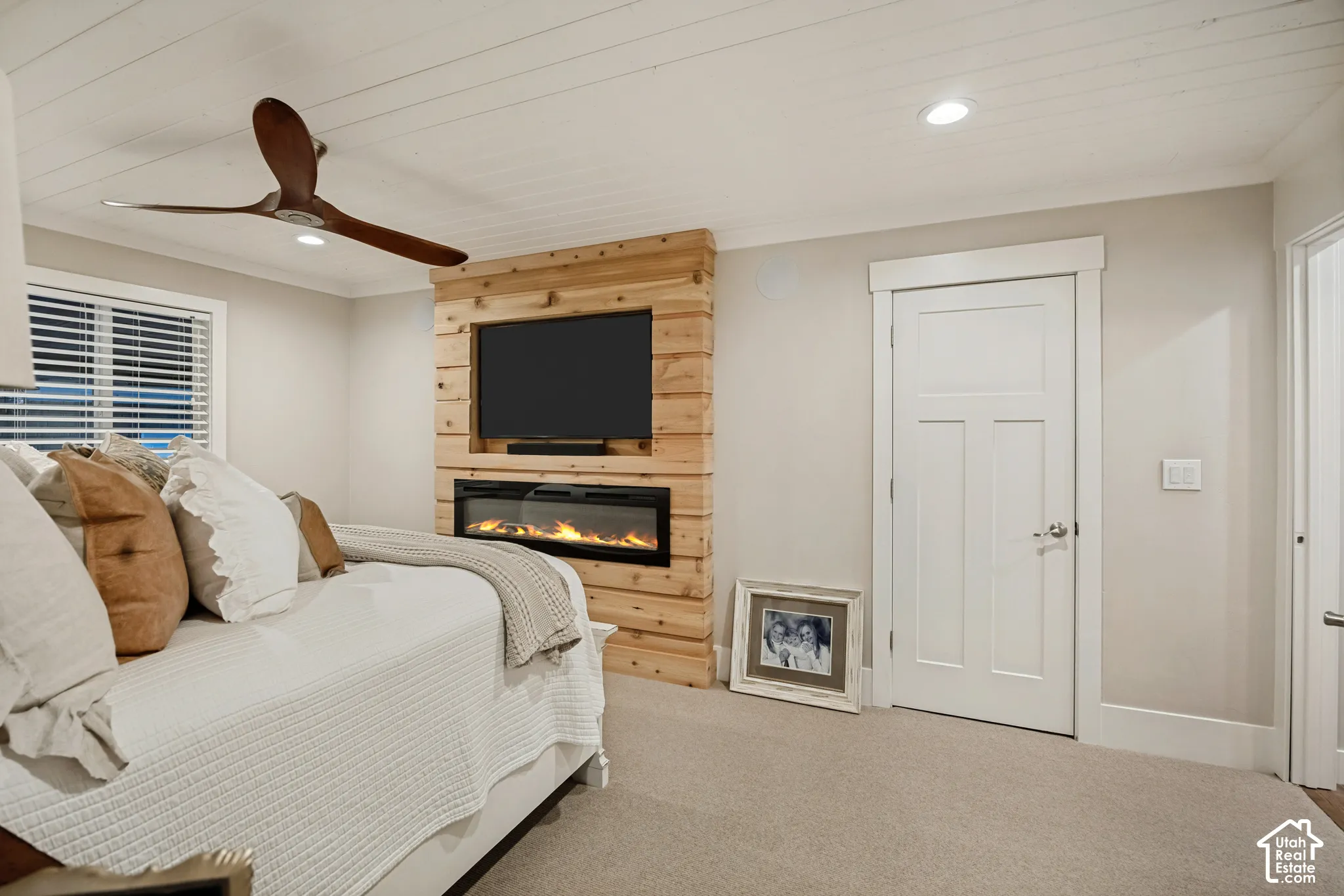 Shiplap ceiling with recessed lighting, integrated wood-finish media wall, built-in electric fireplace, contemporary ceiling fan, and paneled interior door