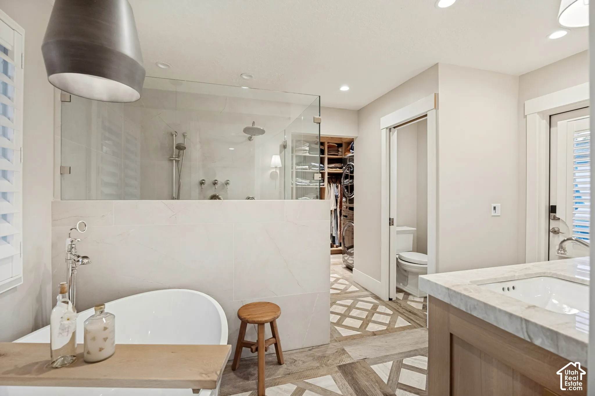 Freestanding soaking tub, walk-in shower with clear glass enclosure, custom built-in closet system, single vanity with integrated sink and stone countertop, and decorative heated floor tiling