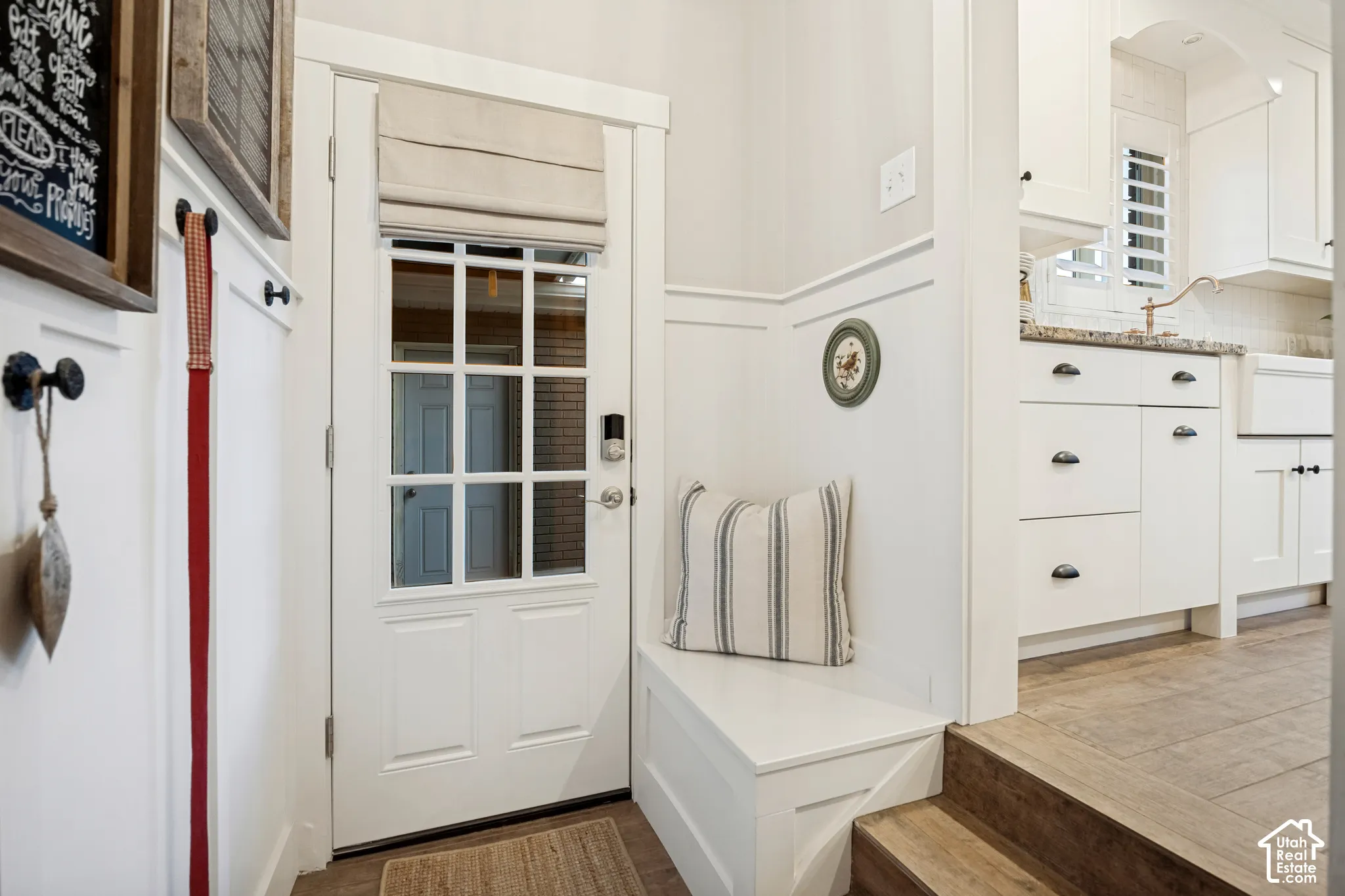 Paneled entry door with transom window, built-in mudroom bench, wall paneling, and wood-finish flooring
