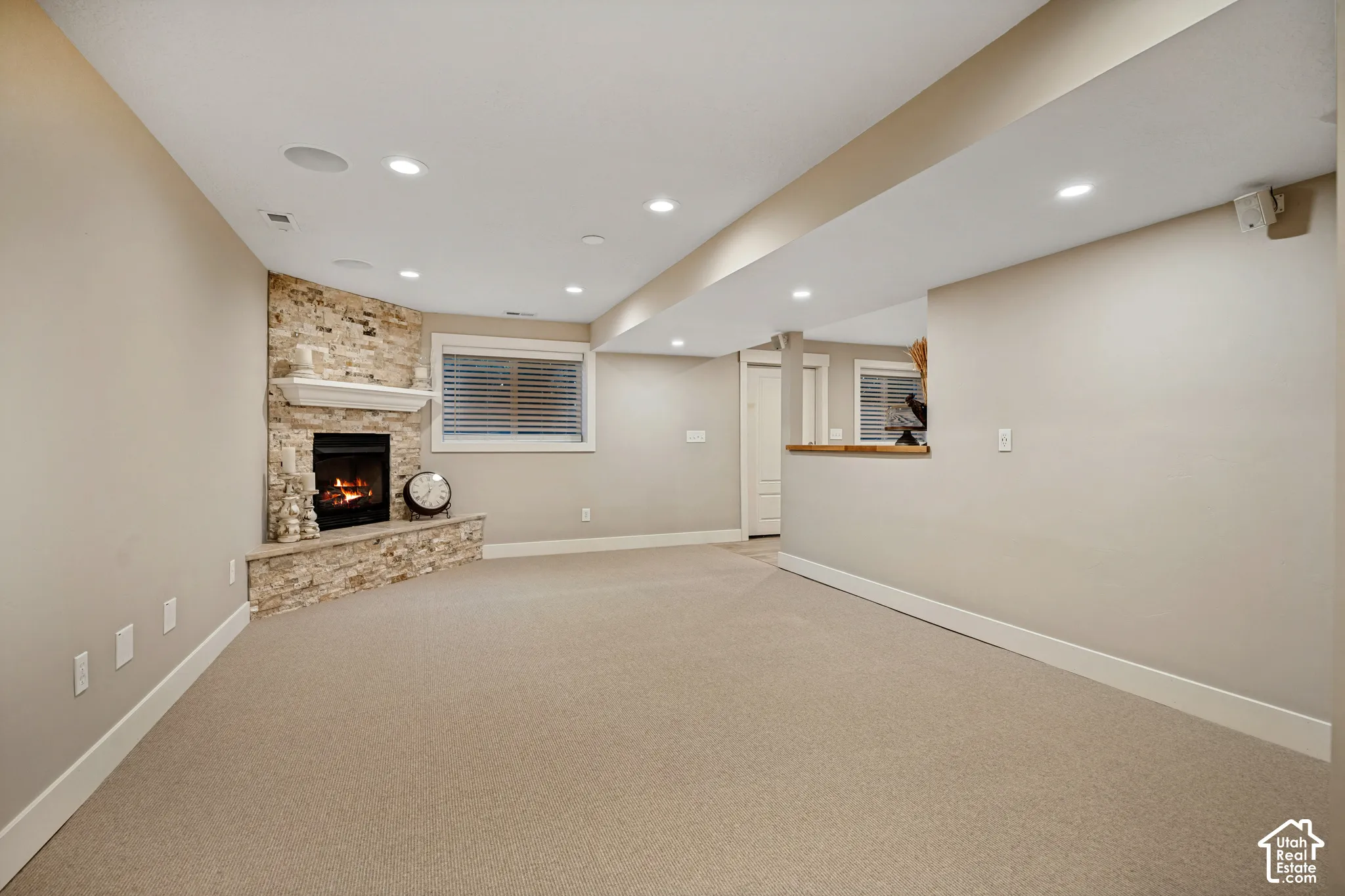 Recessed lighting illuminates the carpeted living area with a stone-clad corner fireplace and hearth