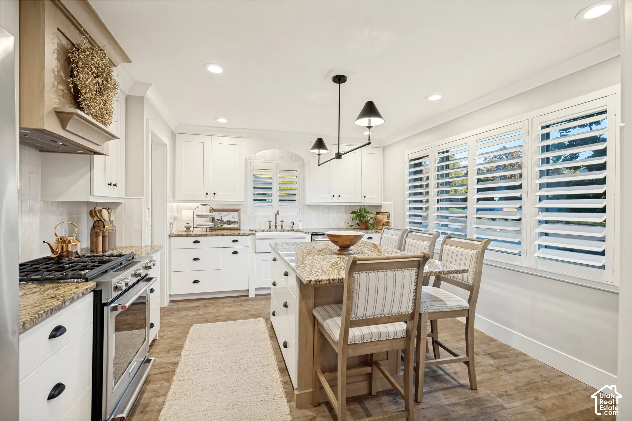 White shaker cabinetry, stainless steel range, light-toned wood-finish flooring, recessed lighting, and a multi-light pendant fixture