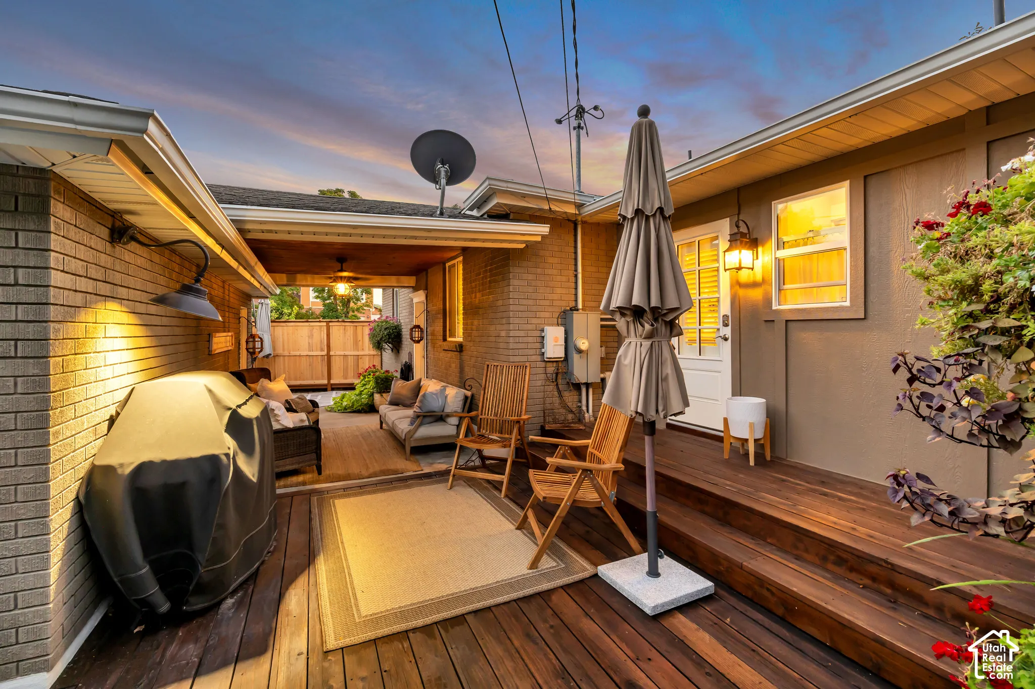 Multi-level wood-finish deck with built-in overhead lighting, brick exterior, and a privacy fence
