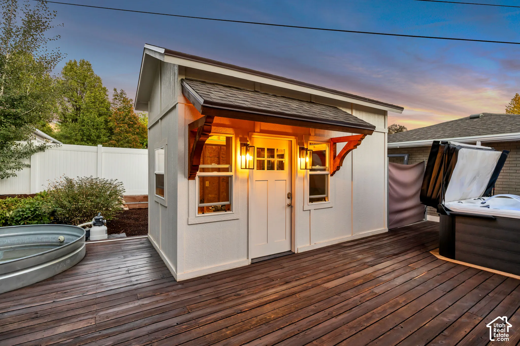Expansive wood-finish deck featuring a detached shed with exterior lighting and a hot tub