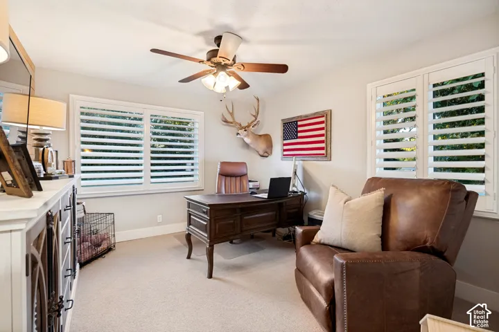 Ceiling fan, two windows with white plantation shutters, and a built-in white cabinet with decorative wood-finish doors