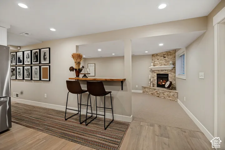 Recessed lighting throughout, wood-finish flooring, built-in bar, stone fireplace surround, and a neutral color palette