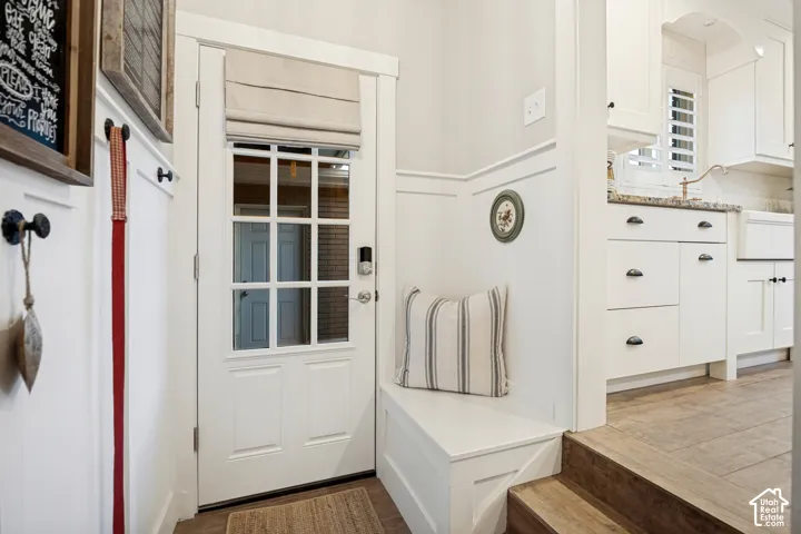 Paneled entry door with transom window, built-in mudroom bench, wall paneling, and wood-finish flooring