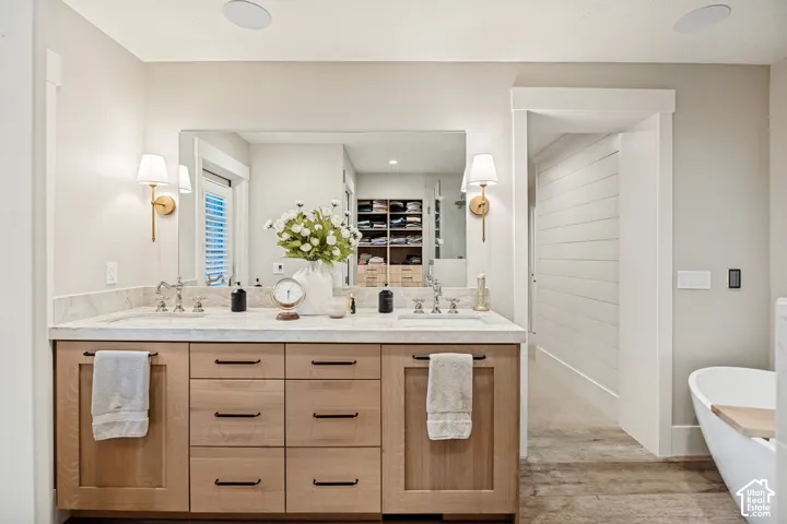 Dual vanity with light wood-finish cabinetry, stone countertop, and brushed brass sconces