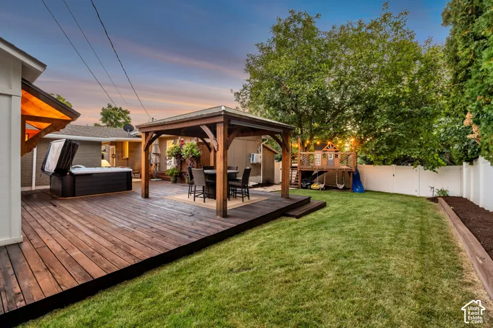 Expansive backyard featuring a wood deck, built-in hot tub, and a wood gazebo with a paved floor