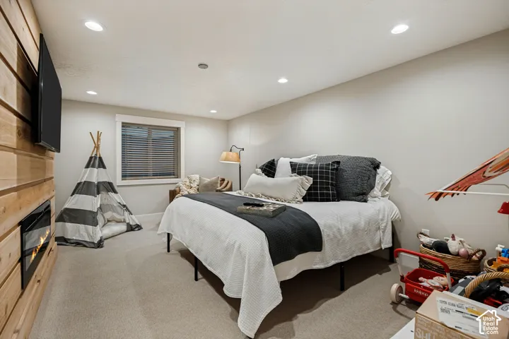 Recessed lighting, wood-paneled wall with built-in fireplace, natural light from the window, and carpeted flooring