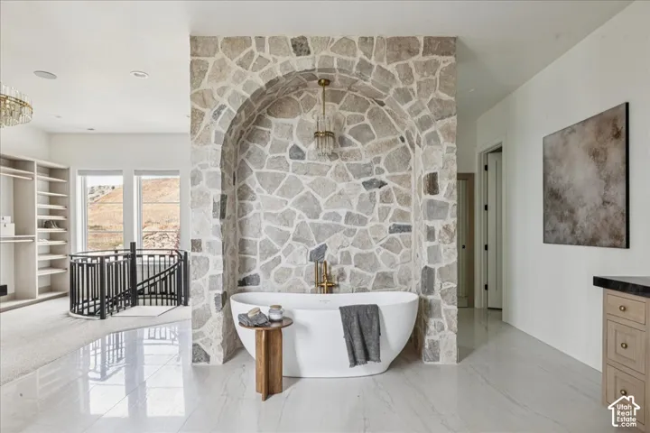 Freestanding tub within a stone-clad arch feature, light-toned flooring, built-in shelving, and a black wrought-iron railing