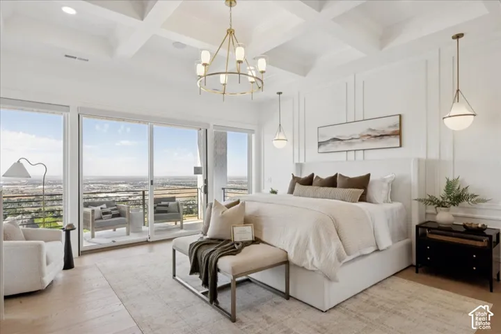 Coffered ceiling with a central chandelier, expansive sliding glass doors, white paneled wall detailing, wood-finish flooring, and a private balcony