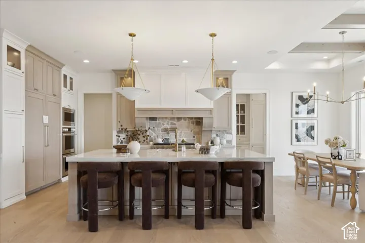 Spacious kitchen island with seating, built-in double ovens, stone backsplash, and recessed lighting