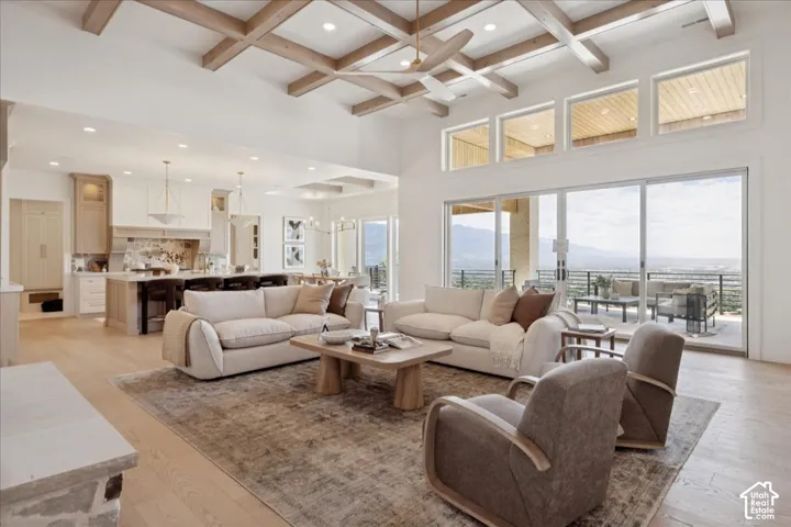 Vaulted ceiling with wood-beam detailing, expansive sliding glass doors, hardwood flooring, and a kitchen featuring an island with seating
